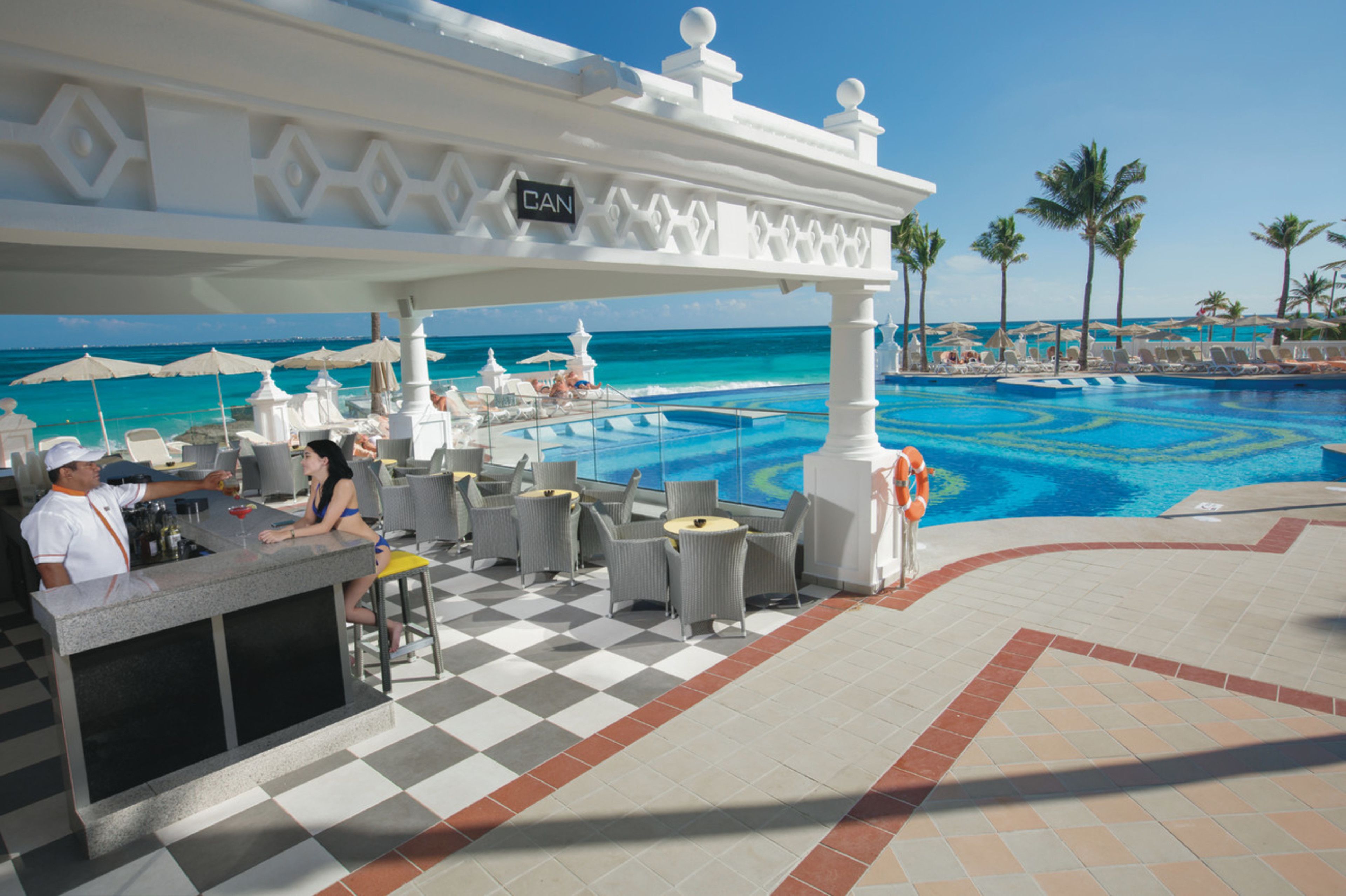 A poolside bar area with a checkered floor, white bar counter, and outdoor seating.