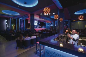 A bar area with a bartender, round tables, and hanging decorative lights.