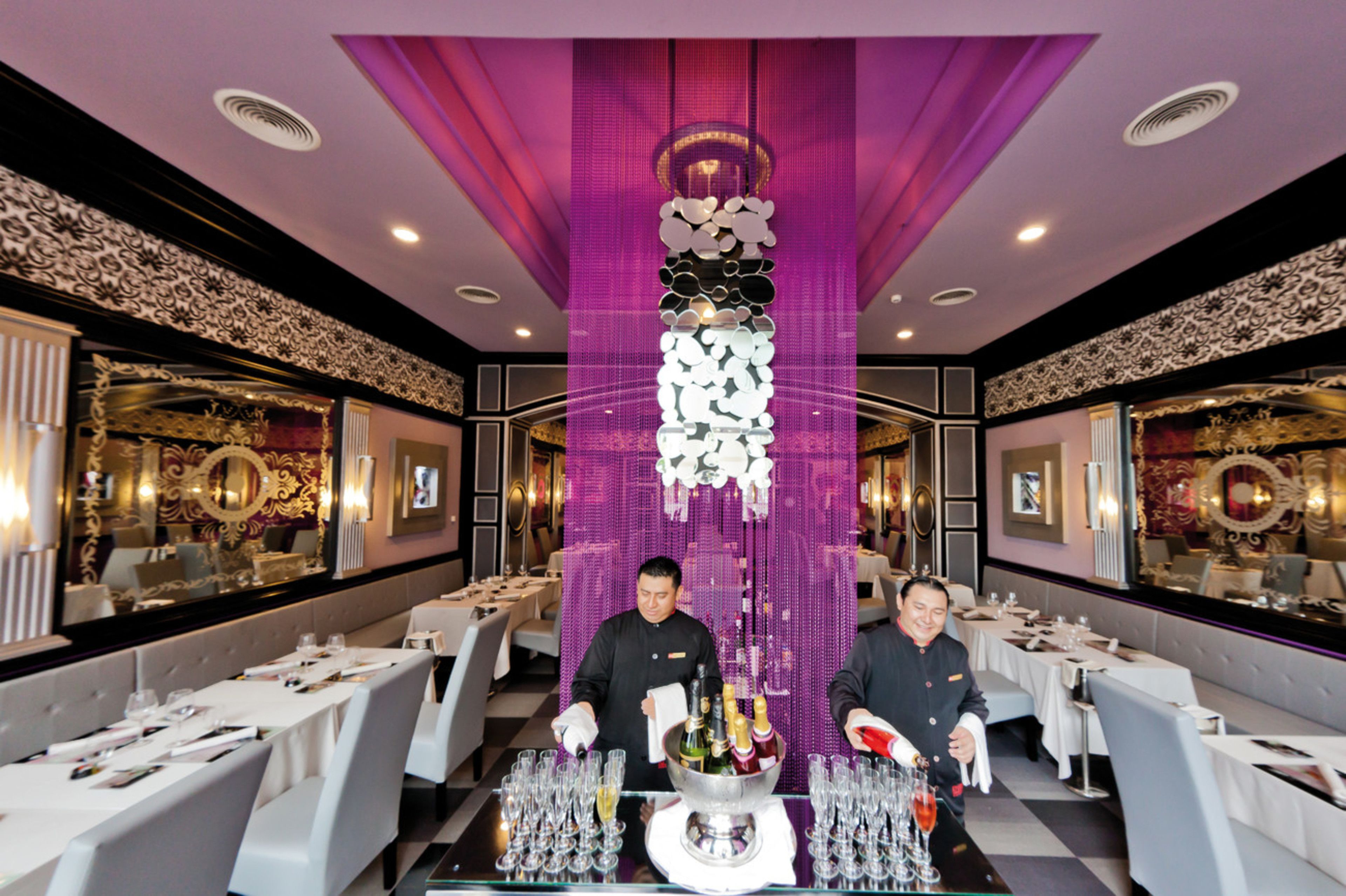Un restaurante con barra central, varias mesas y una estructura decorativa colgante.