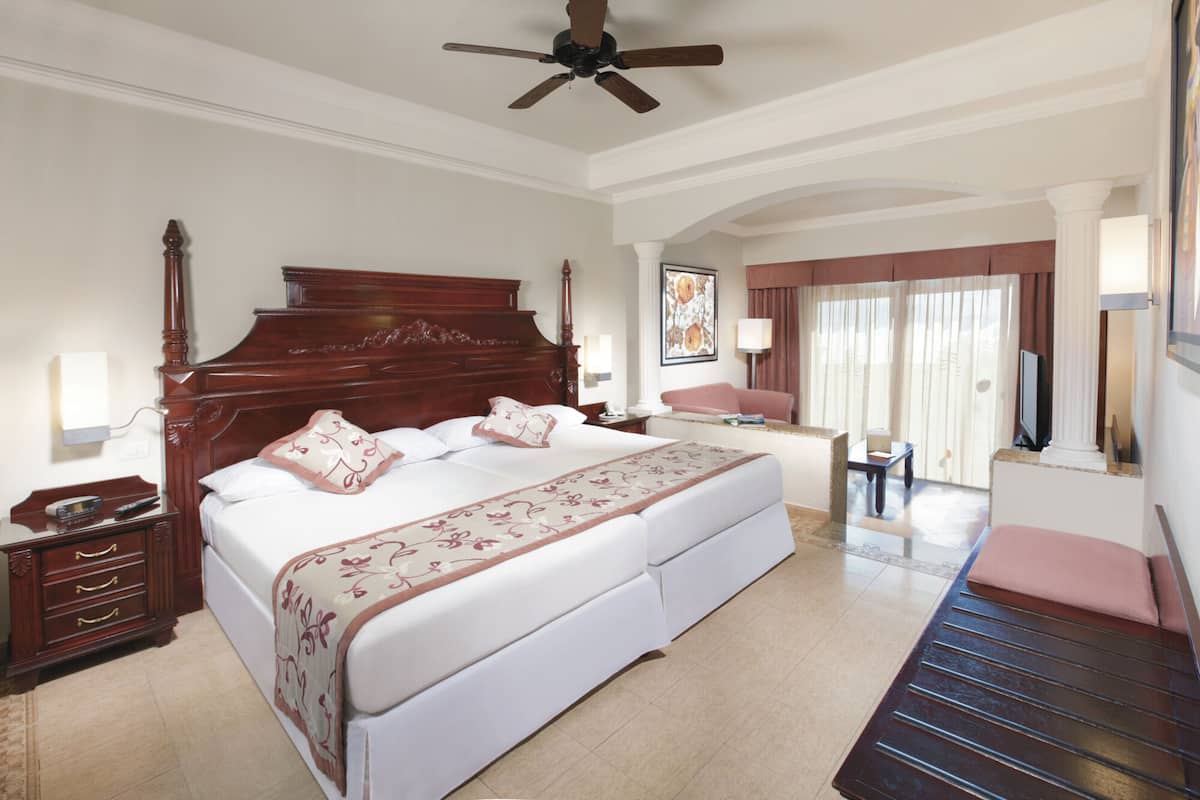 A hotel room with a large bed, a desk, a chair, a television, and a ceiling fan.