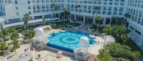 A hotel courtyard with a central pool, palm trees, and a large building in the background.