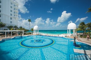 A resort pool with a star design, palm trees, and a beach view.