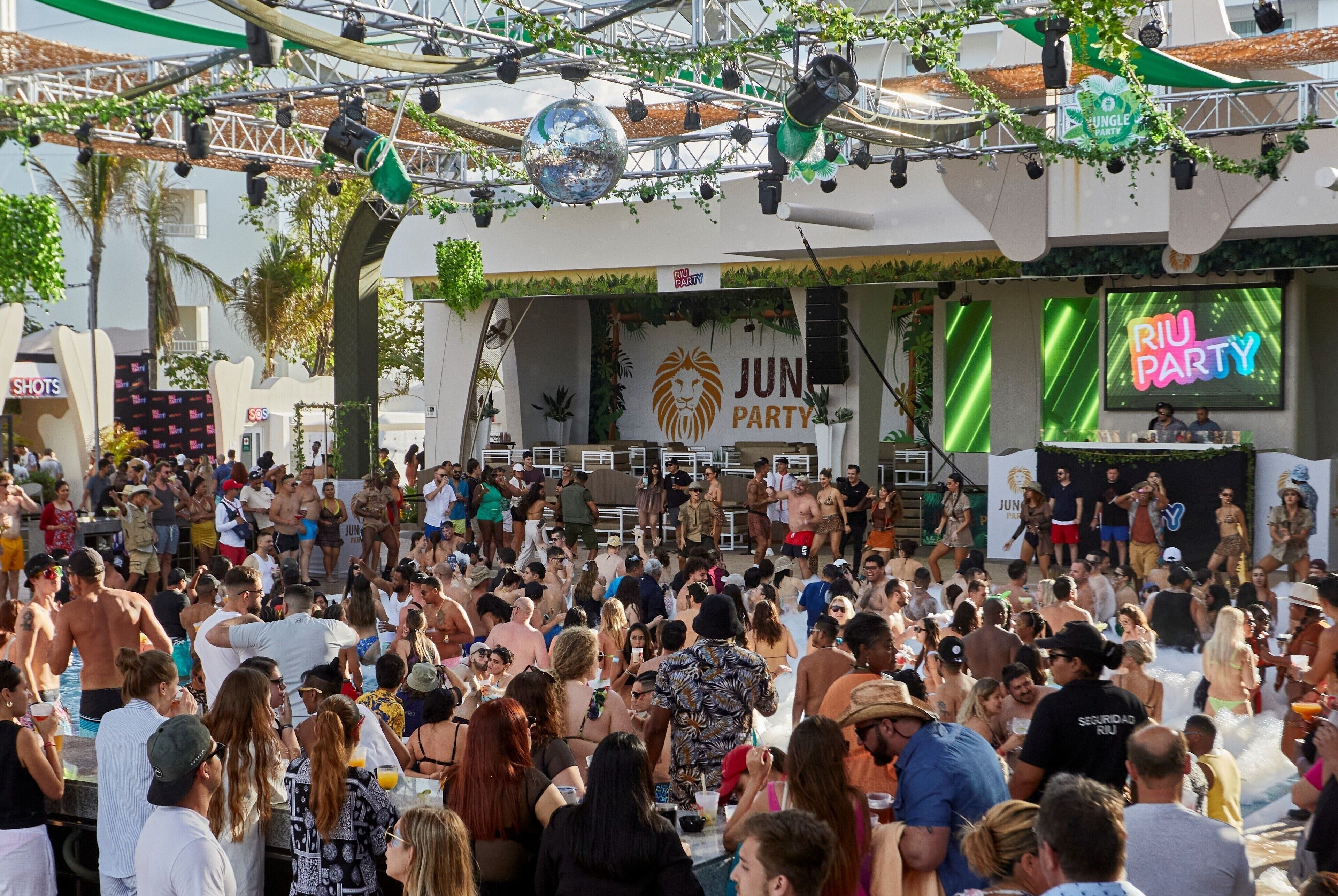 A crowded outdoor event with a stage and a DJ booth.
