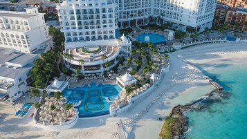 Vista aérea de un resort con varias piscinas, una playa y un gran edificio hotelero.