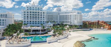 Um grande resort com vários edifícios, uma área de piscina central e uma praia com águas turquesa cristalinas.