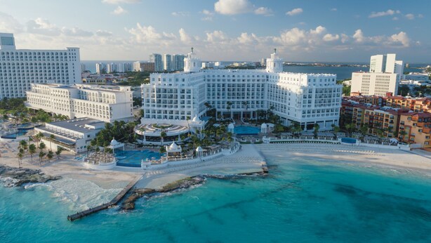 A large resort with multiple buildings, a central pool, and a beach area.