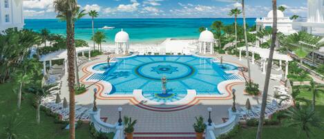 Un resort con piscina central, palmeras y vista al océano.