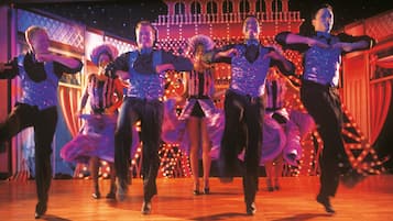 A group of dancers performing on a wooden floor with a decorative backdrop.