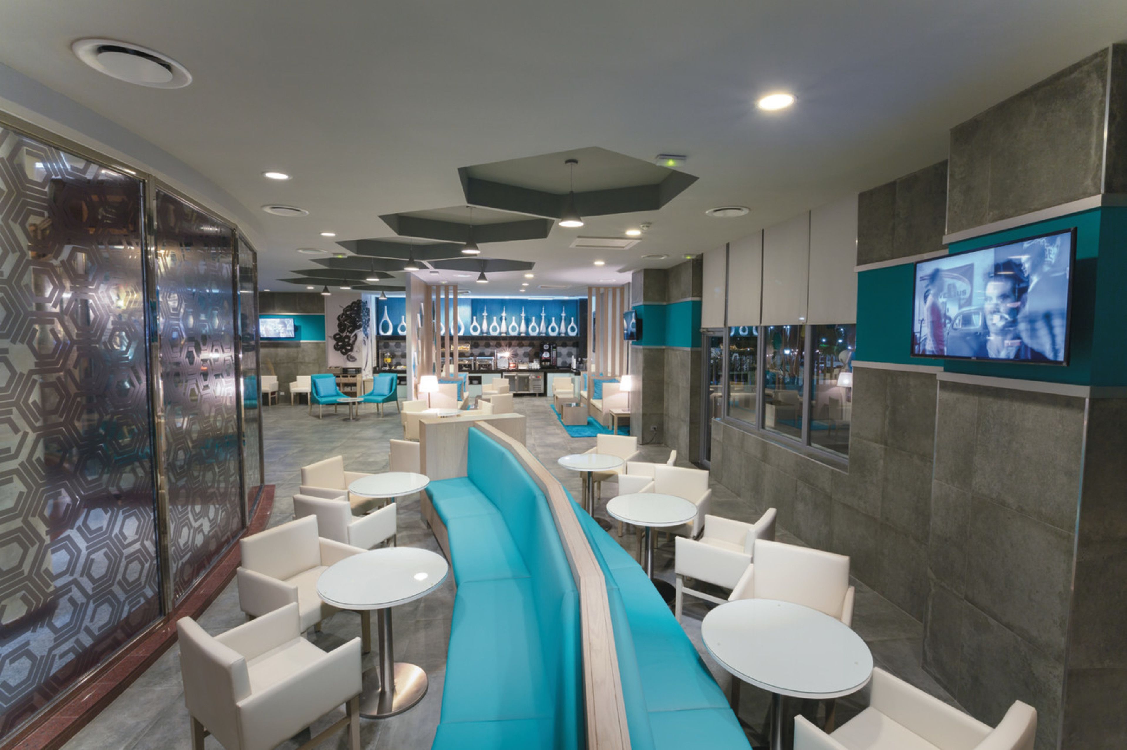 Un espace de détente moderne avec des sièges disposés en arc de cercle, un bar et un écran de télévision fixé au mur.