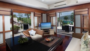 Una sala de estar moderna con televisor, asientos cómodos, una mesita de centro con fruta y ventanas amplias que ofrecen vistas al exterior.