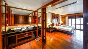 Un dormitorio amplio con una cama grande, un baño independiente con lavamanos doble y vistas al exterior a través de amplios ventanales.