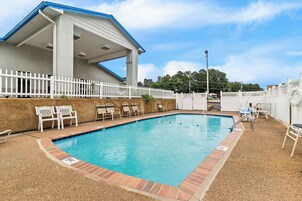 A swimming pool with a white fence, lounge chairs, and a covered area with a blue roof.