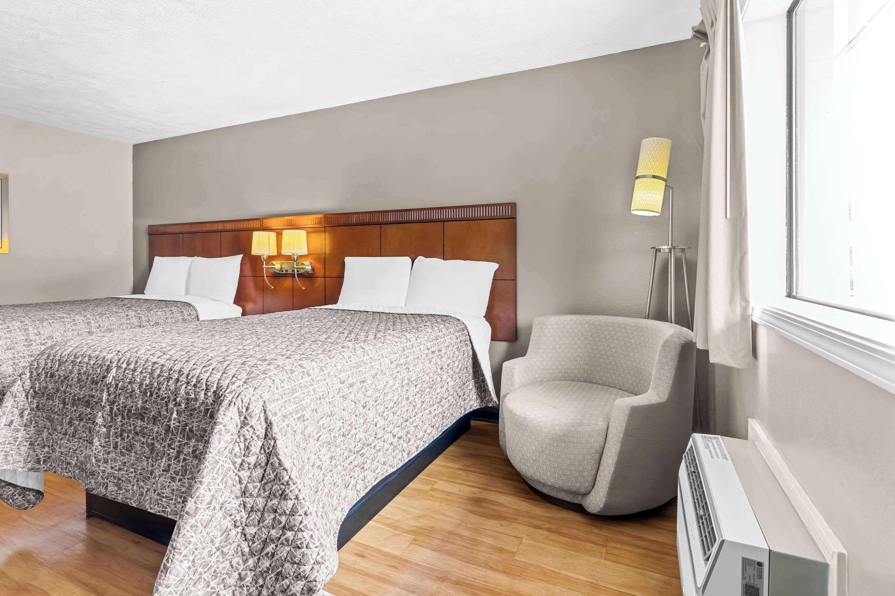 A hotel room with a large bed, a chair, a bedside table, a lamp, and a window.