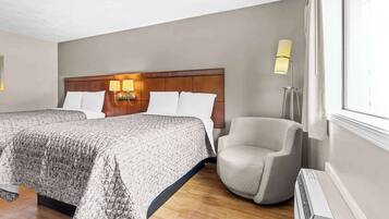 A hotel room with a large bed, a chair, a bedside table, a lamp, and a window.