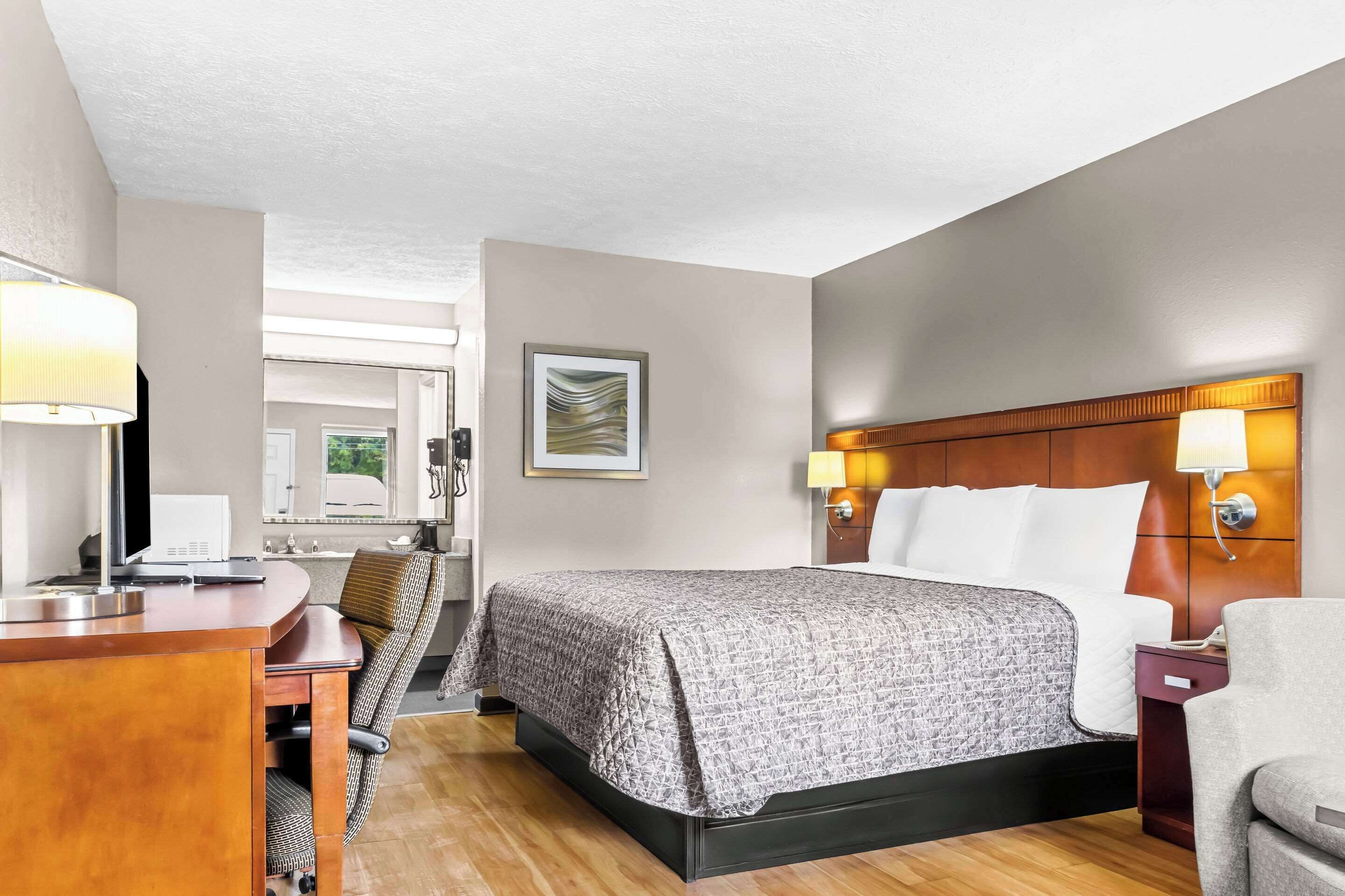 Habitación de hotel con cama, escritorio, silla y lámparas de noche.