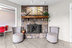 Uma sala de estar moderna com lareira de pedra, duas poltronas cinzas, uma cadeira vermelha e uma estante de madeira com plantas.