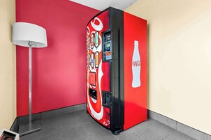 A Coca-Cola branded vending machine in a room with red walls and a floor lamp.