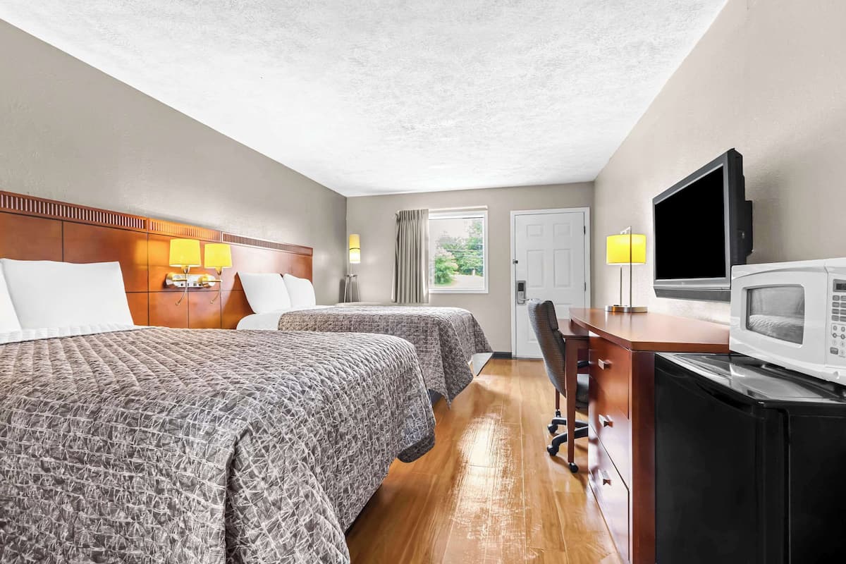 A hotel room with two beds, a desk with a TV, a microwave, and a window with curtains.