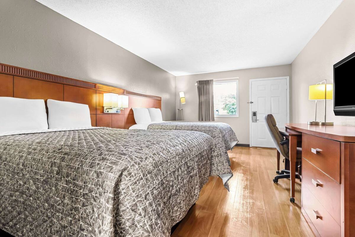 A hotel room with two beds, a desk, a chair, a TV, and a window with curtains.