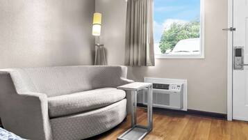 Een moderne hotelkamer met een grijze bank, een kleine tafel, een verticale heater en een raam met gordijnen.