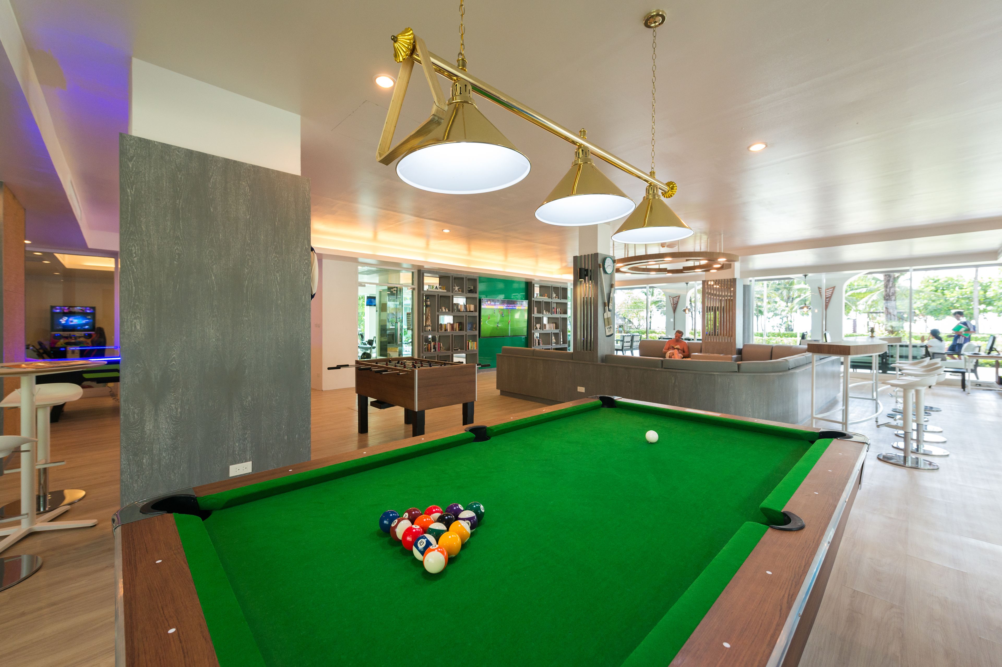 Une table de billard recouverte d’un drap vert et dotée de différentes billes de couleurs. On aperçoit un bar avec des tabourets et un comptoir au fond.