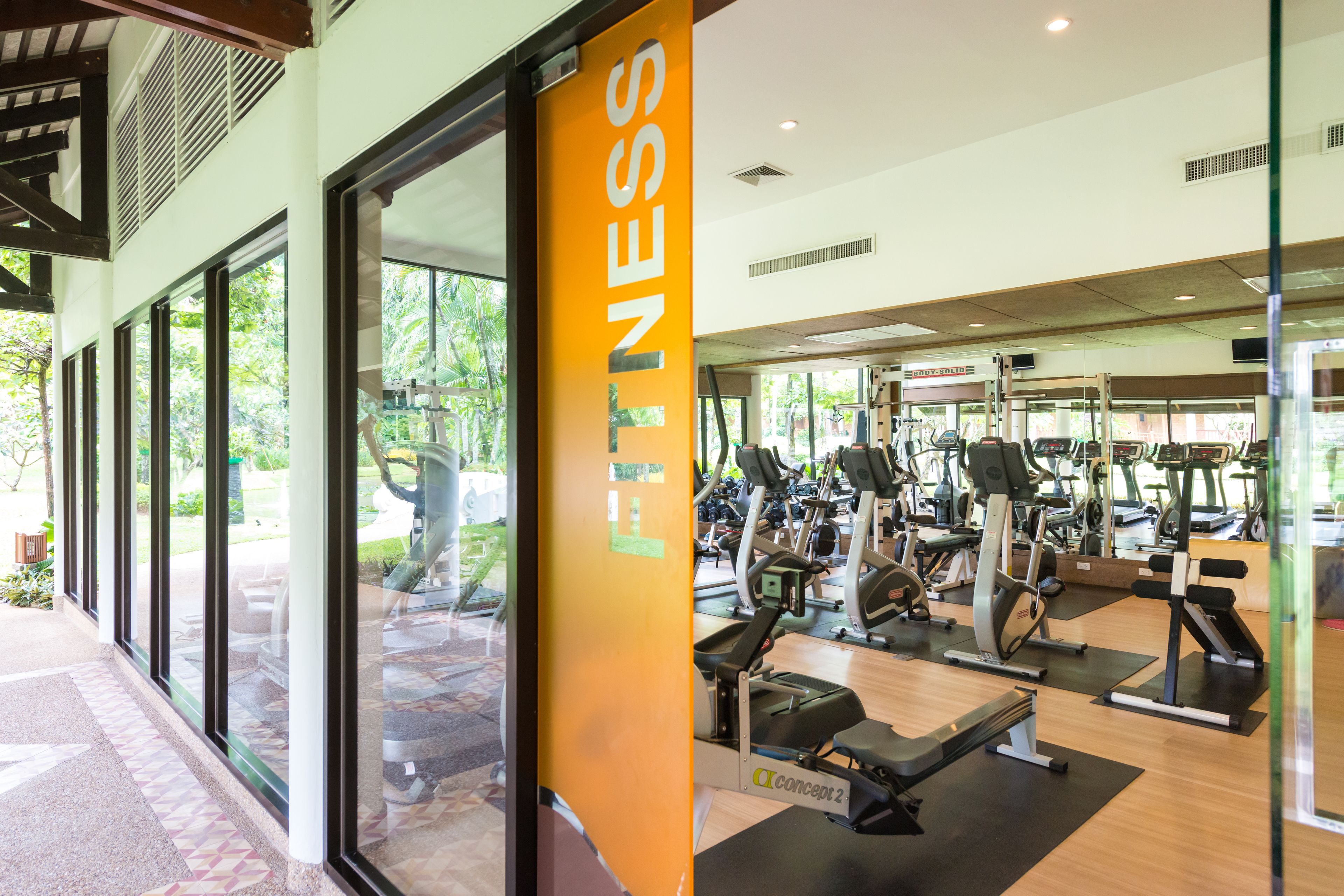 A gym with various exercise equipment, large windows, and a sign that reads "FITNESS".