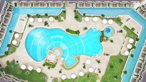 An aerial view of a resort with a large central swimming pool, multiple smaller pools, and numerous sun loungers and umbrellas. - Katathani Phuket Beach Resort (Karon)