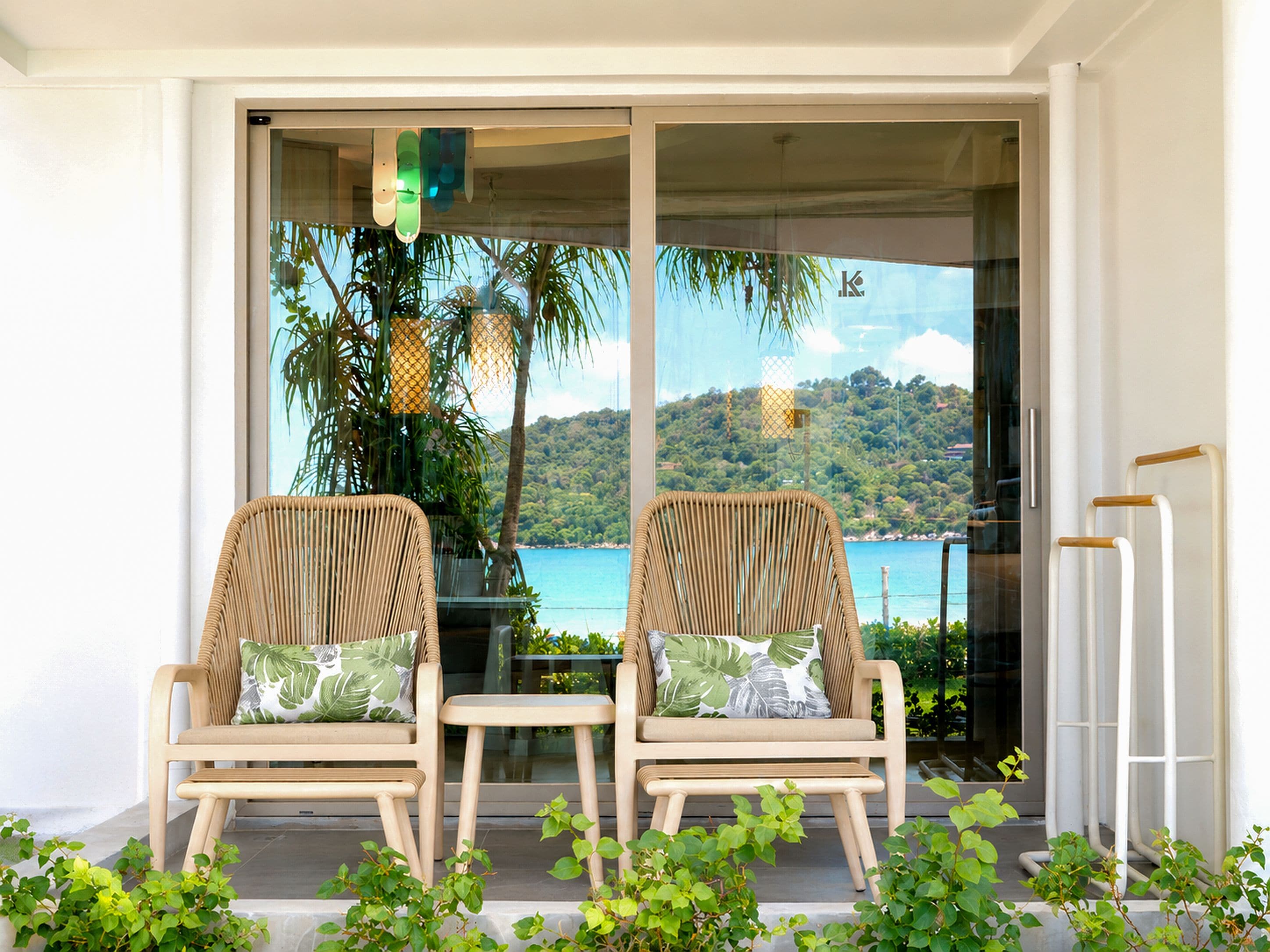 Two wicker chairs with cushions, a small table, and a view of a coastal landscape through a glass door.