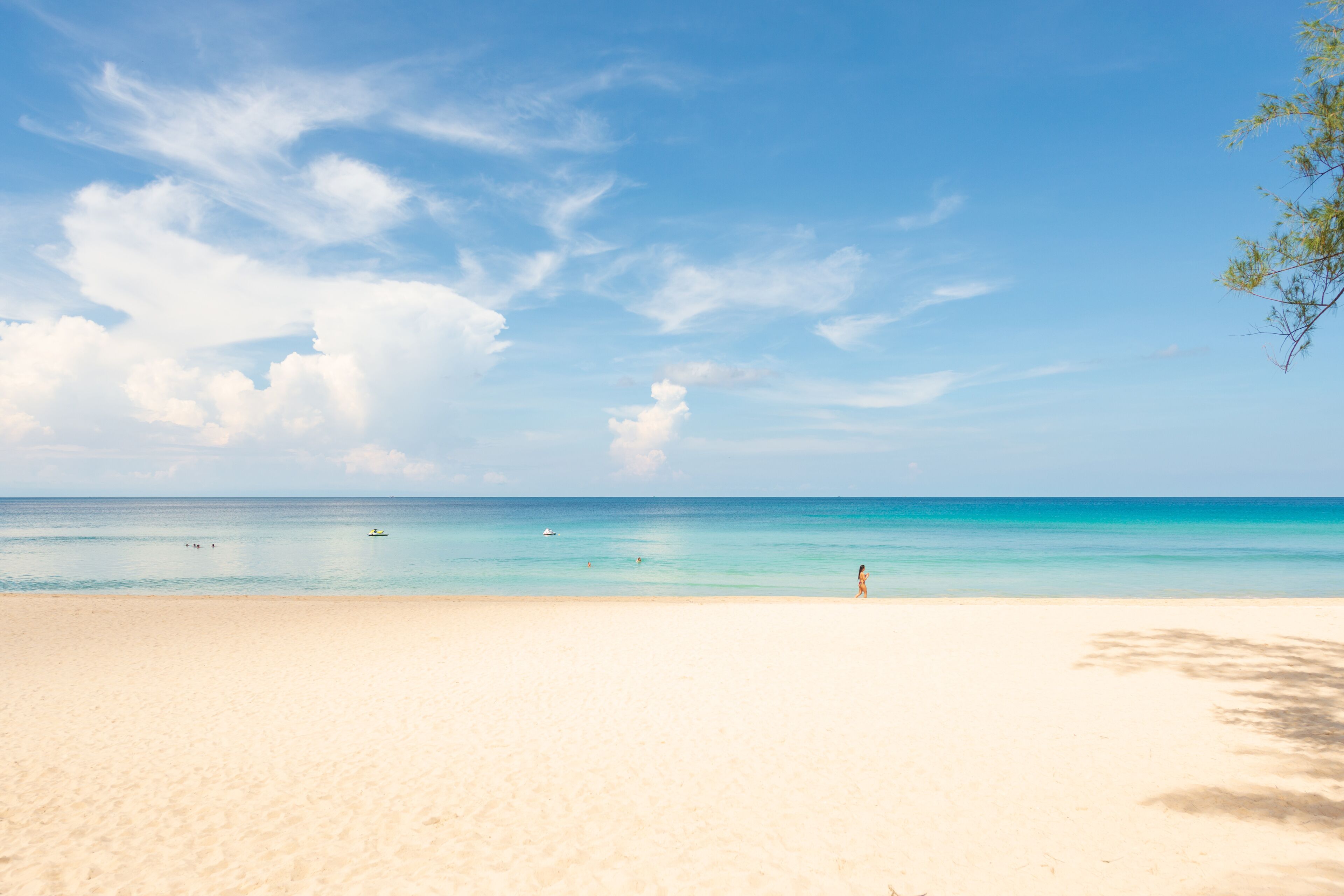 A beach with clear turquoise water, a sandy shore, and a few people in the distance.