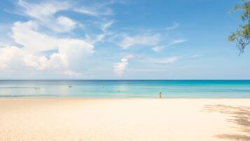 A beach with clear turquoise water, a sandy shore, and a few people in the distance.