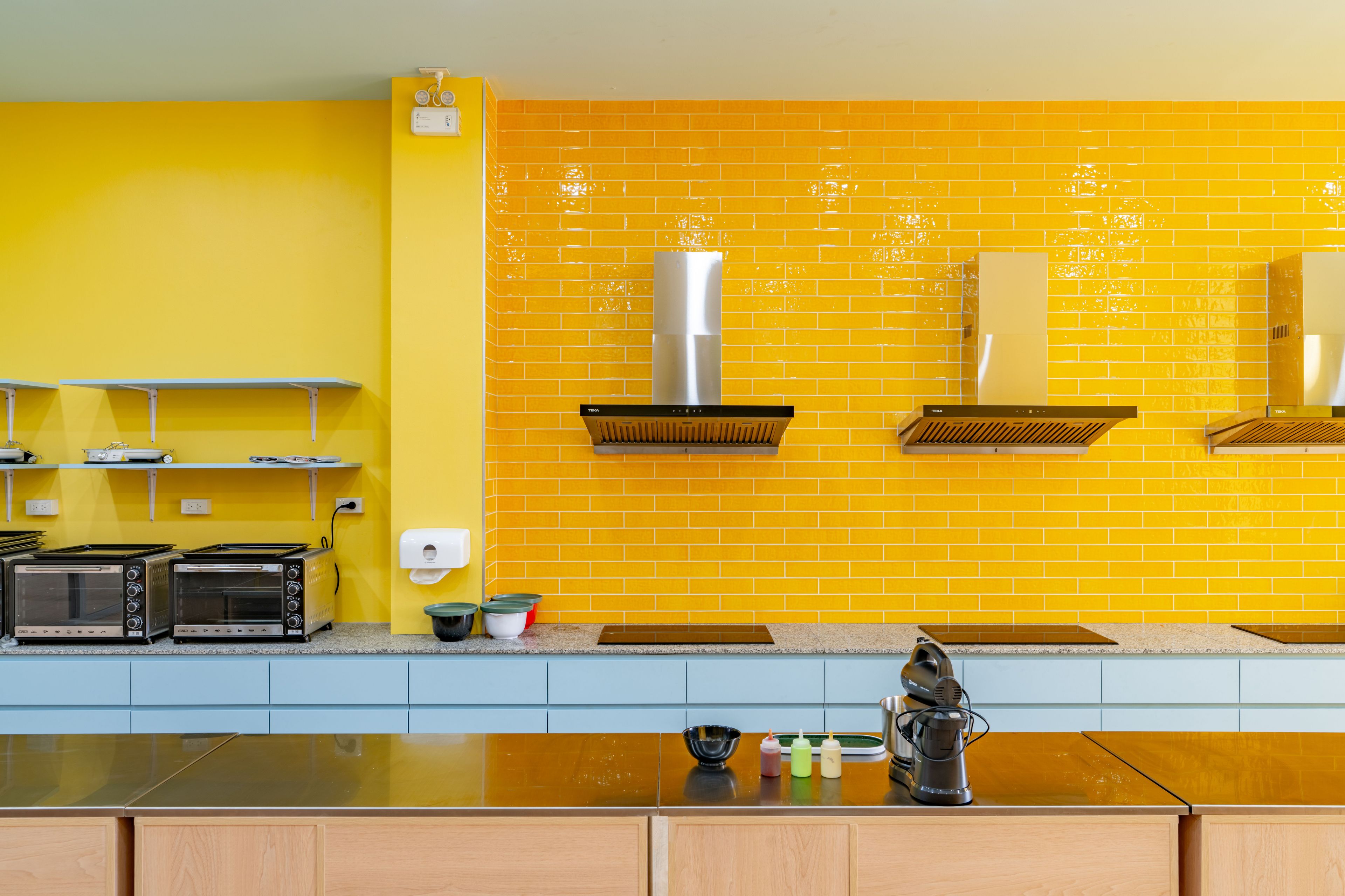A kitchen with yellow walls, two built-in toasters, a sink, and a range hood.