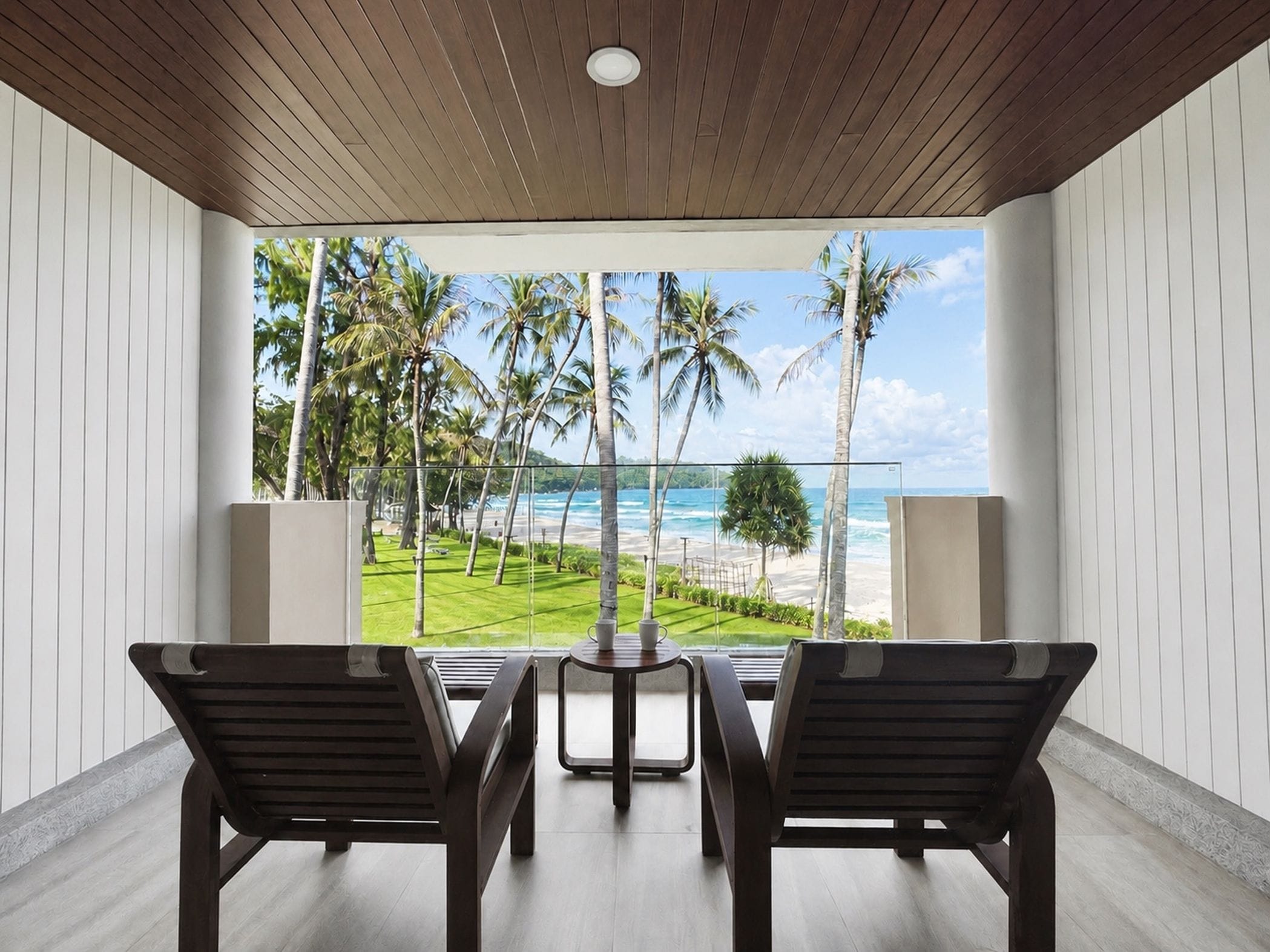 A room with a view of a beach and palm trees. There are two chairs and a small table.