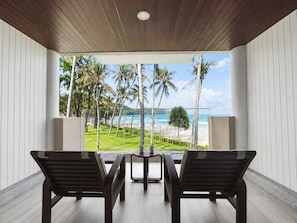 A room with a view of a beach and palm trees. There are two chairs and a small table. - Katathani Phuket Beach Resort (Karon)