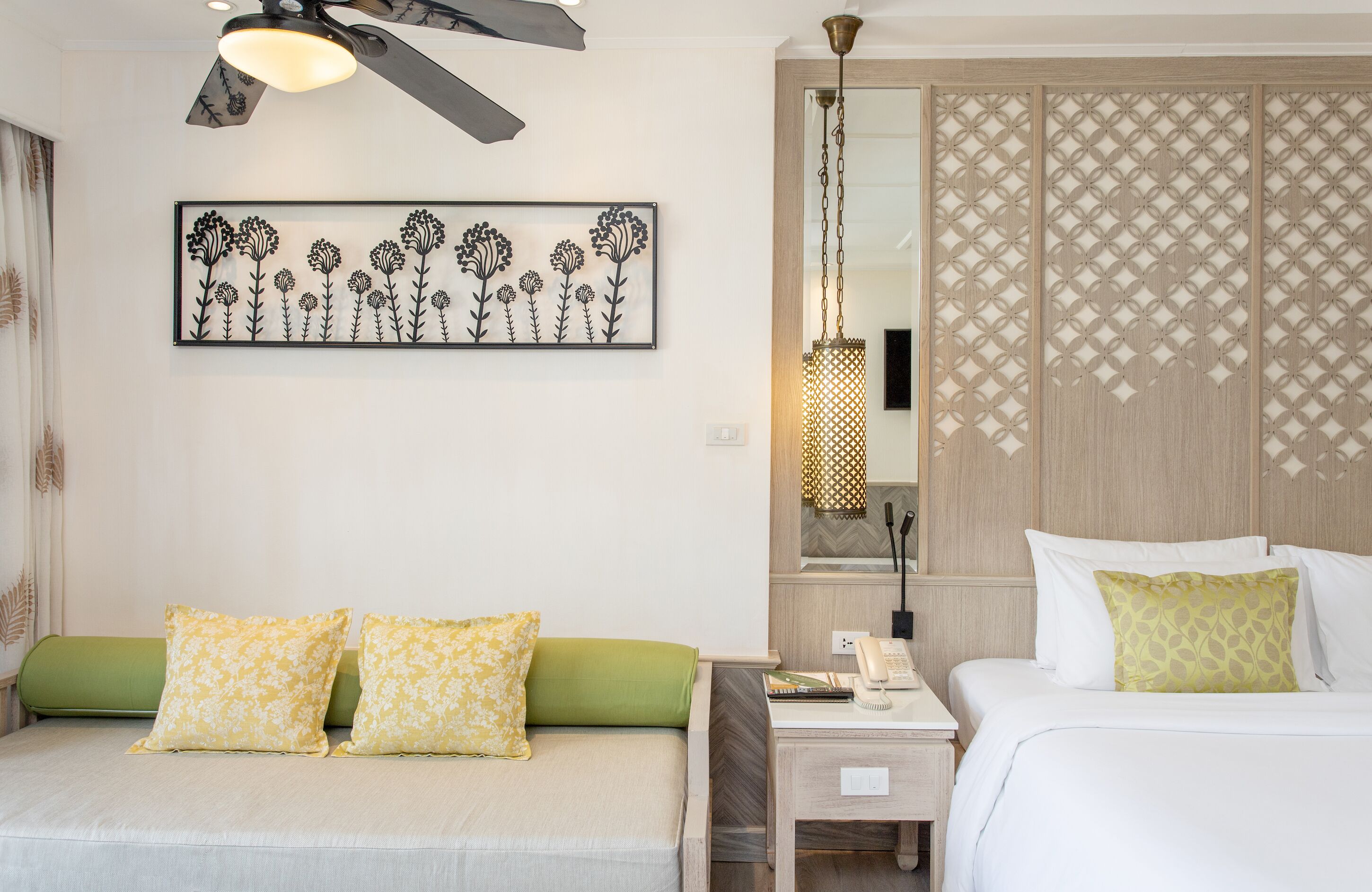 Une chambre d’hôtel comprenant un lit, un canapé, une table de chevet, une lampe et un élément décoratif mural.