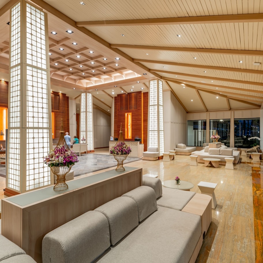 A spacious lobby with a high ceiling, wooden beams, and a central seating area with sofas and a coffee table.