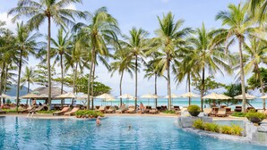 A pool area with lounge chairs, umbrellas, and palm trees. - Katathani Phuket Beach Resort (Karon)