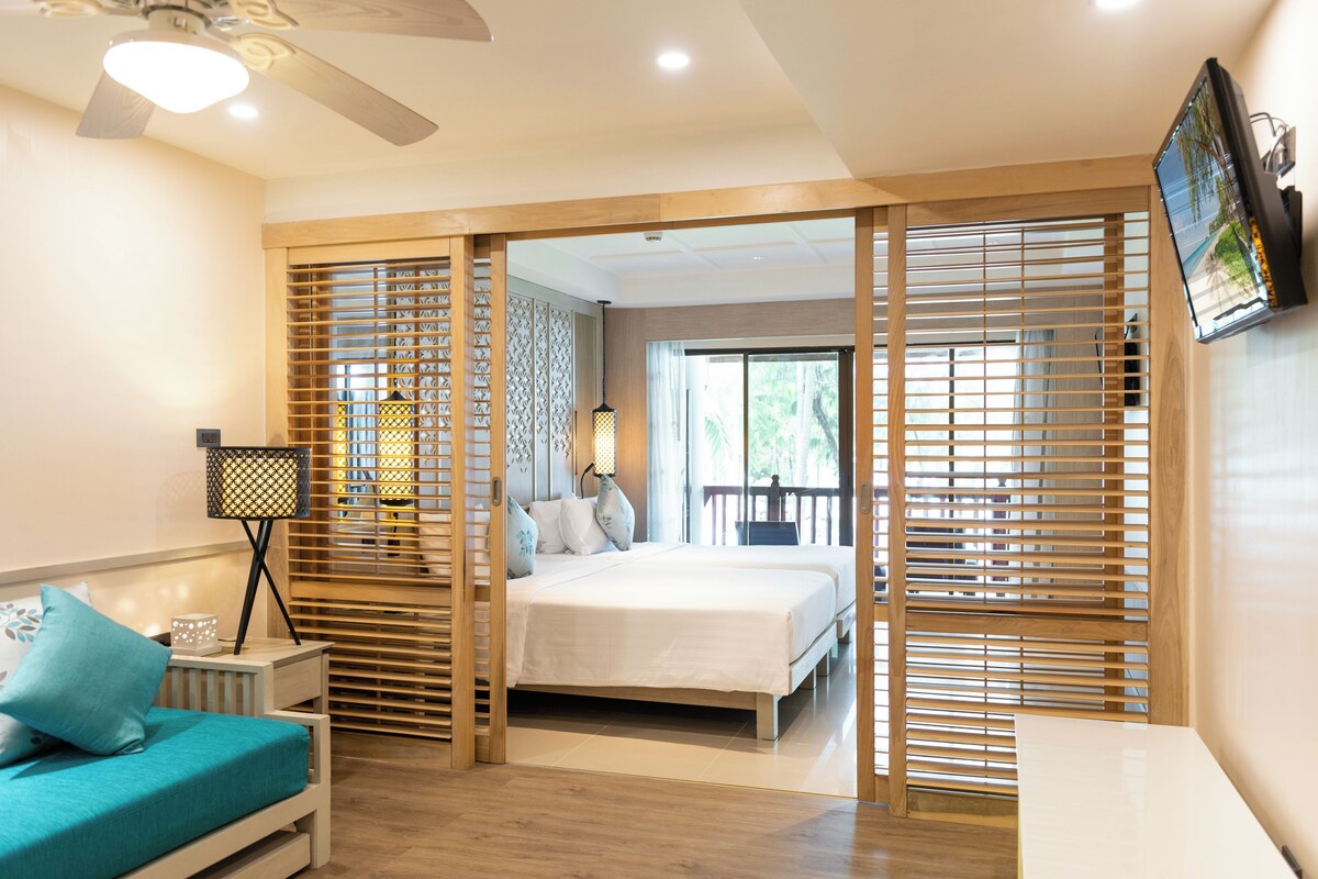 A bedroom with a bed, a nightstand, a desk, a ceiling fan, and a TV mounted on the wall.