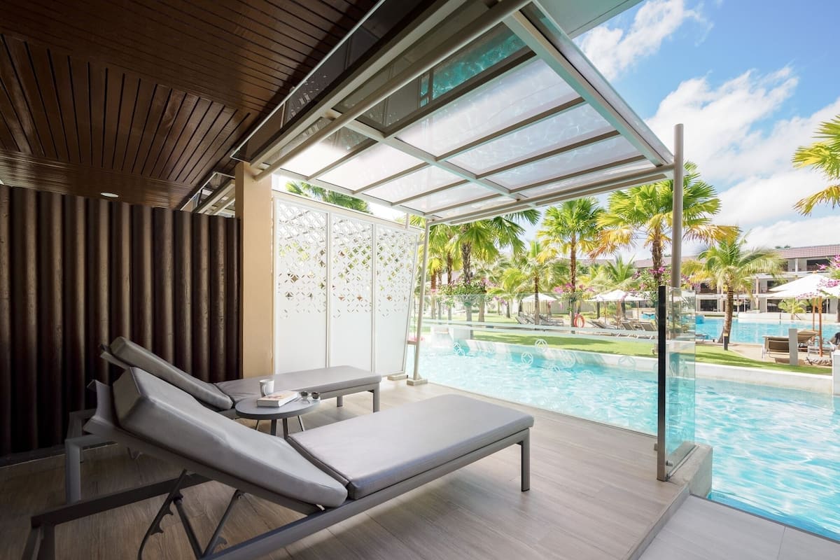 Ein moderner Poolbereich mit Liegestuhl, kleinem Tisch und Blick auf einen Swimmingpool und Palmen.