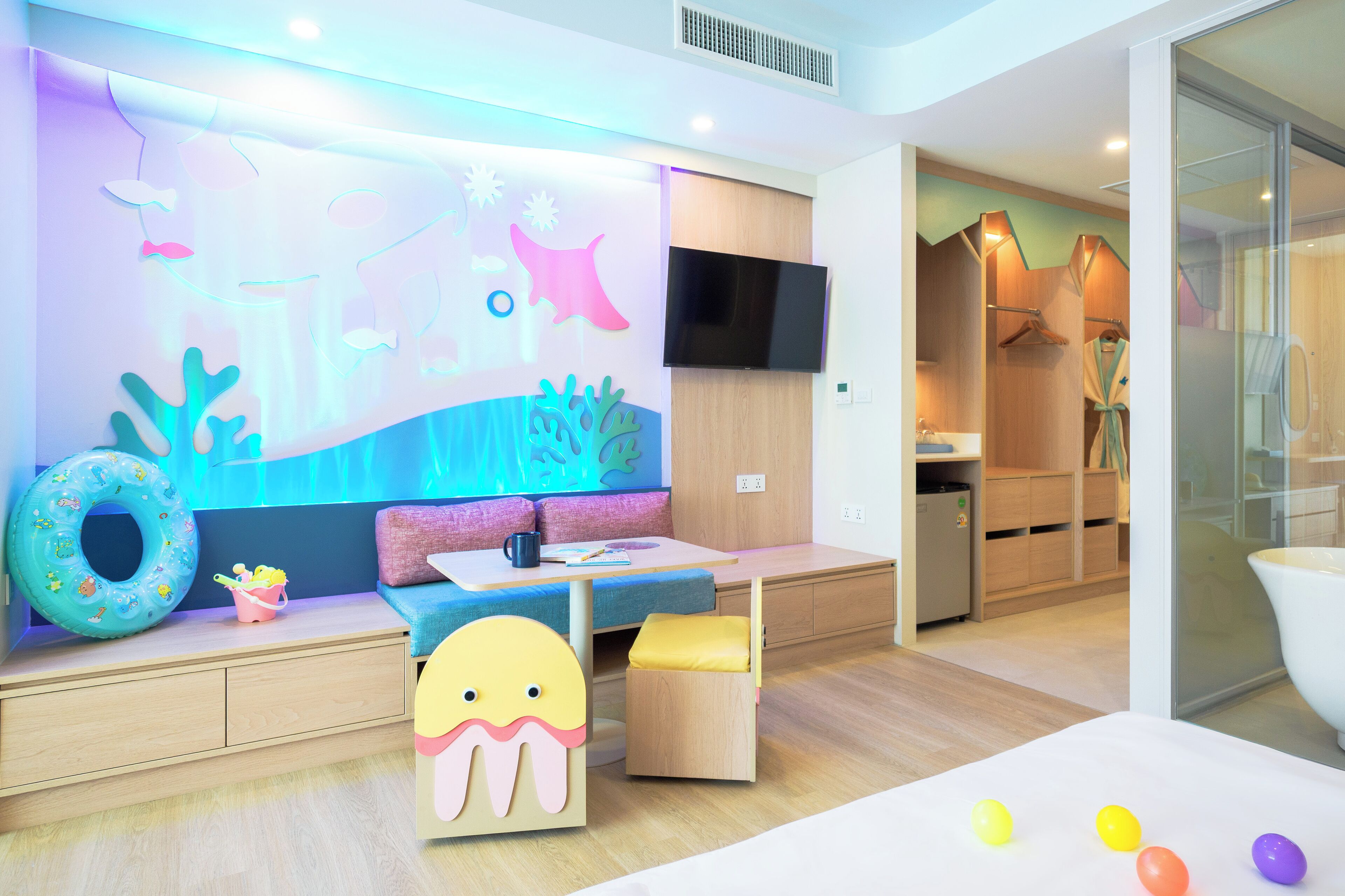 Ein moderner Kinderspielbereich mit Wandgemälde, Sitzgelegenheiten und Fernseher.