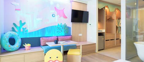 A modern children's play area with a wall mural, seating, and a TV.
