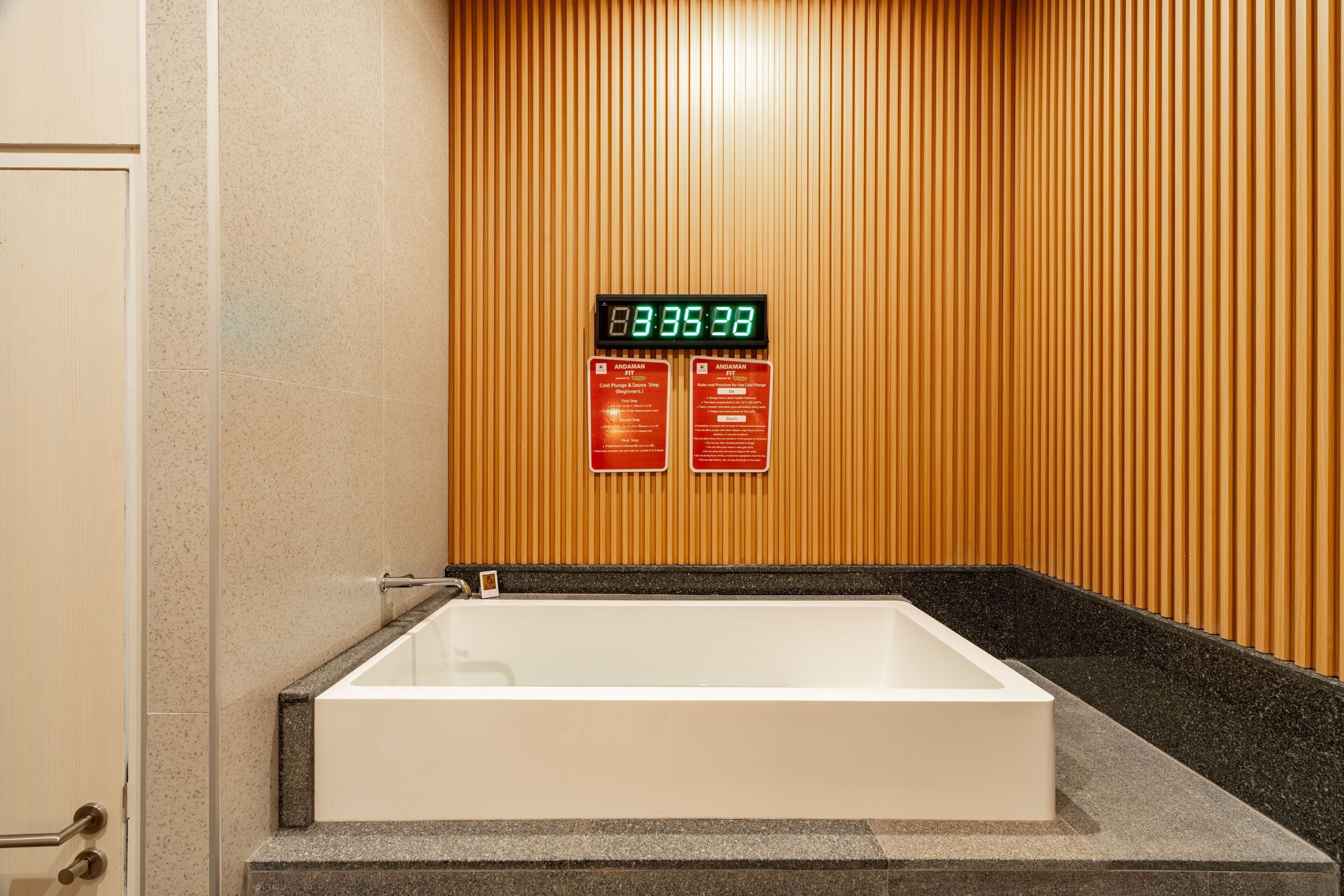 A modern bathroom with a freestanding bathtub, wooden paneling, and a digital clock displaying the time.