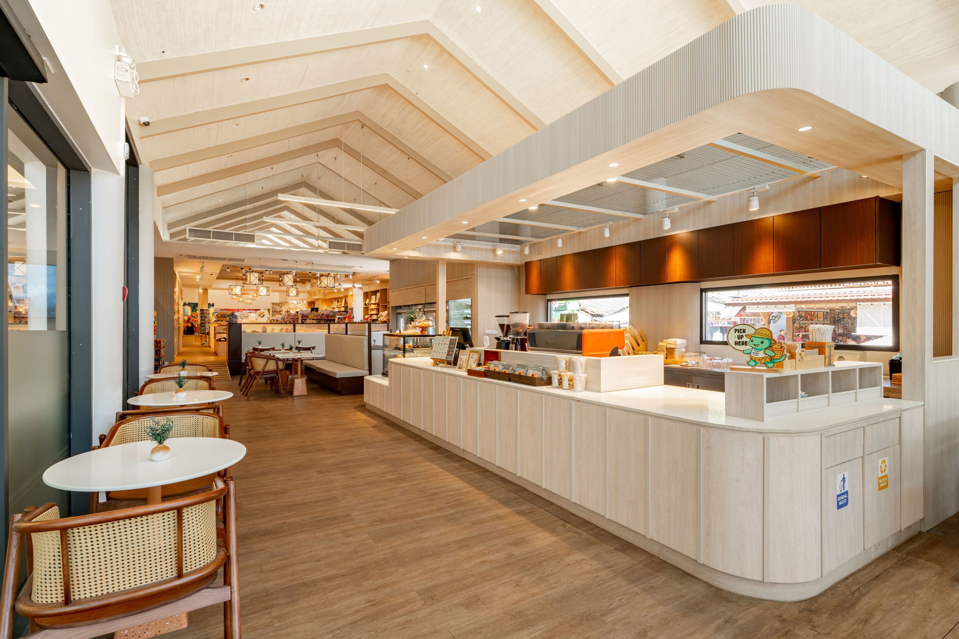 A modern cafe interior with wooden flooring, white counter, and wicker chairs.