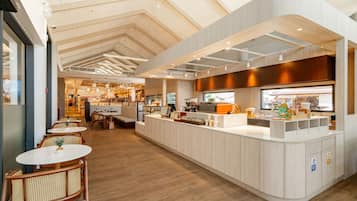 A modern cafe interior with wooden flooring, white counter, and wicker chairs.