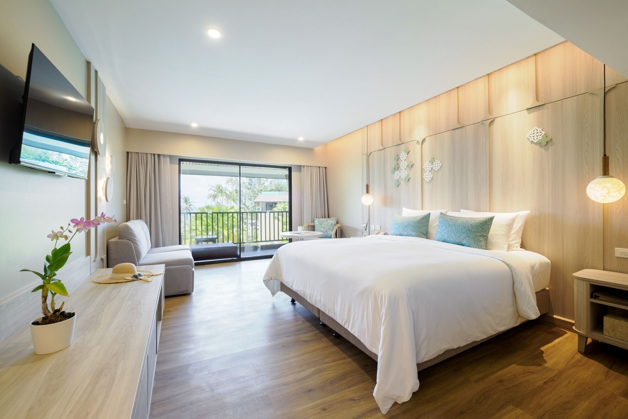 A modern bedroom with a large bed, a sofa, a small table, and a TV mounted on the wall.