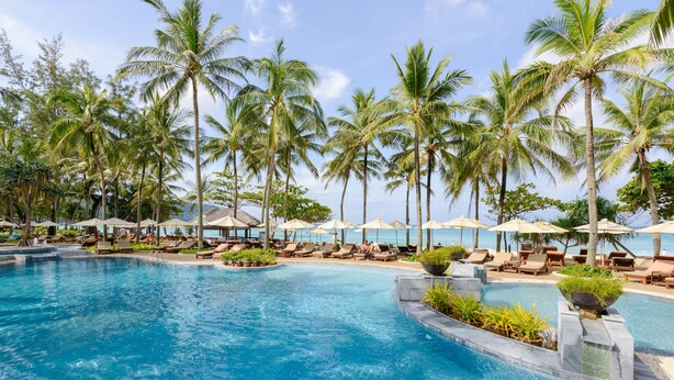 A pool area with lounge chairs and umbrellas, surrounded by palm trees. - Katathani Phuket Beach Resort (Karon)