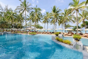 A pool area with lounge chairs and umbrellas, surrounded by palm trees. - Katathani Phuket Beach Resort (Karon)