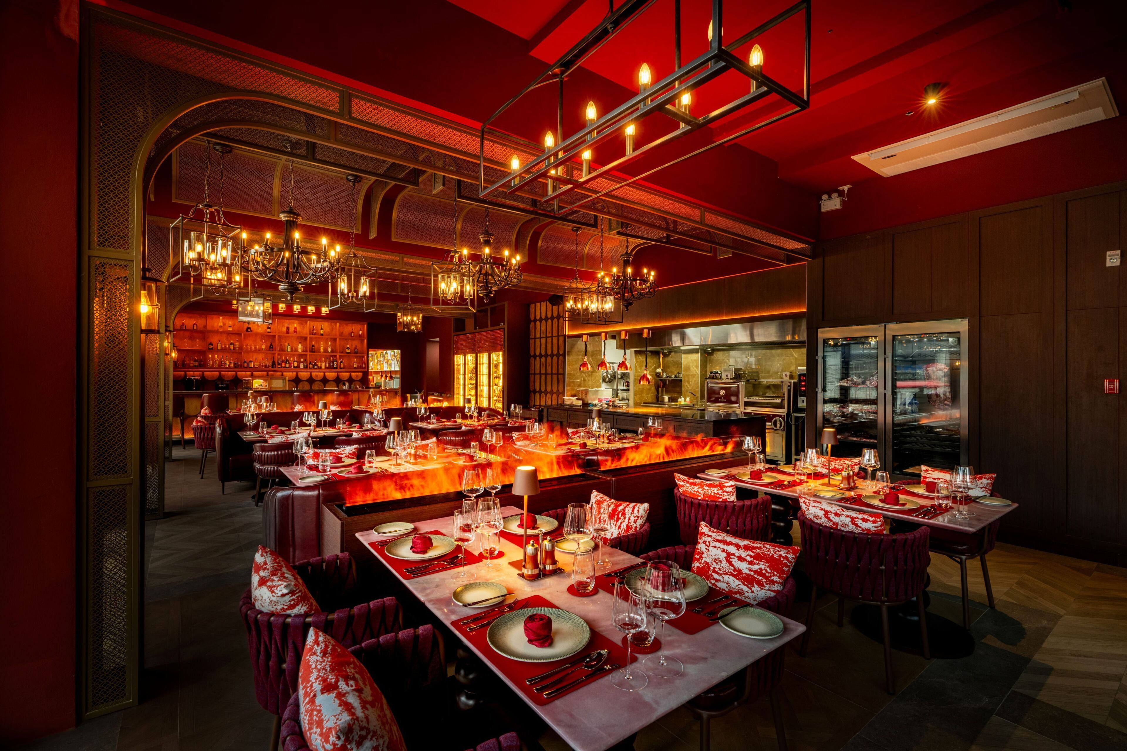 A restaurant with multiple dining tables set for guests, a bar area, and a kitchen visible through the open space.
