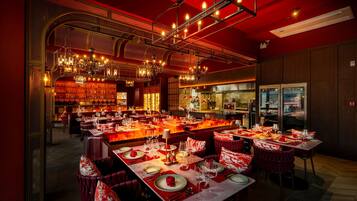 A restaurant with multiple dining tables set for guests, a bar area, and a kitchen visible through the open space.