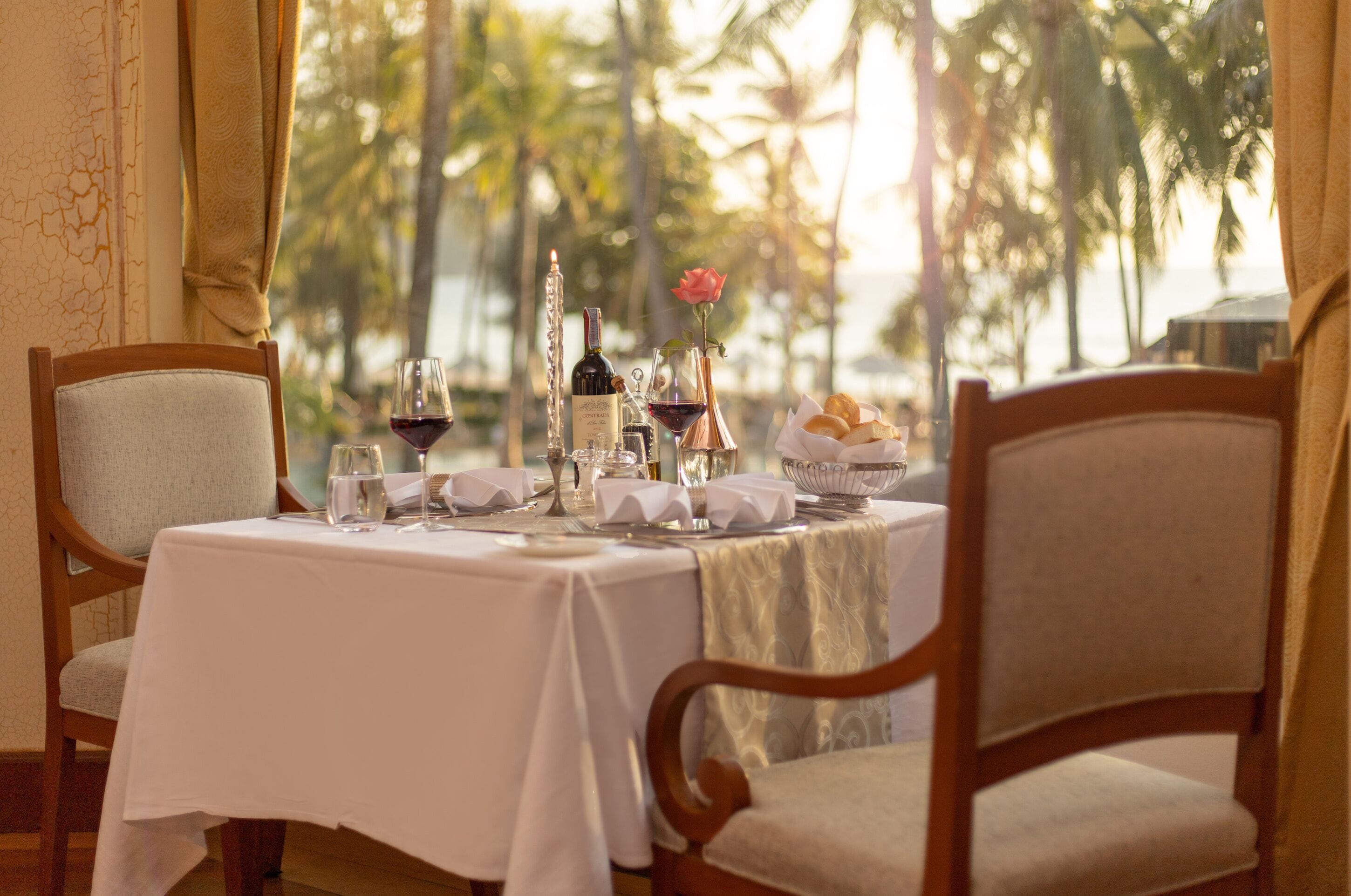 A table set for two with a view of palm trees and the sea.