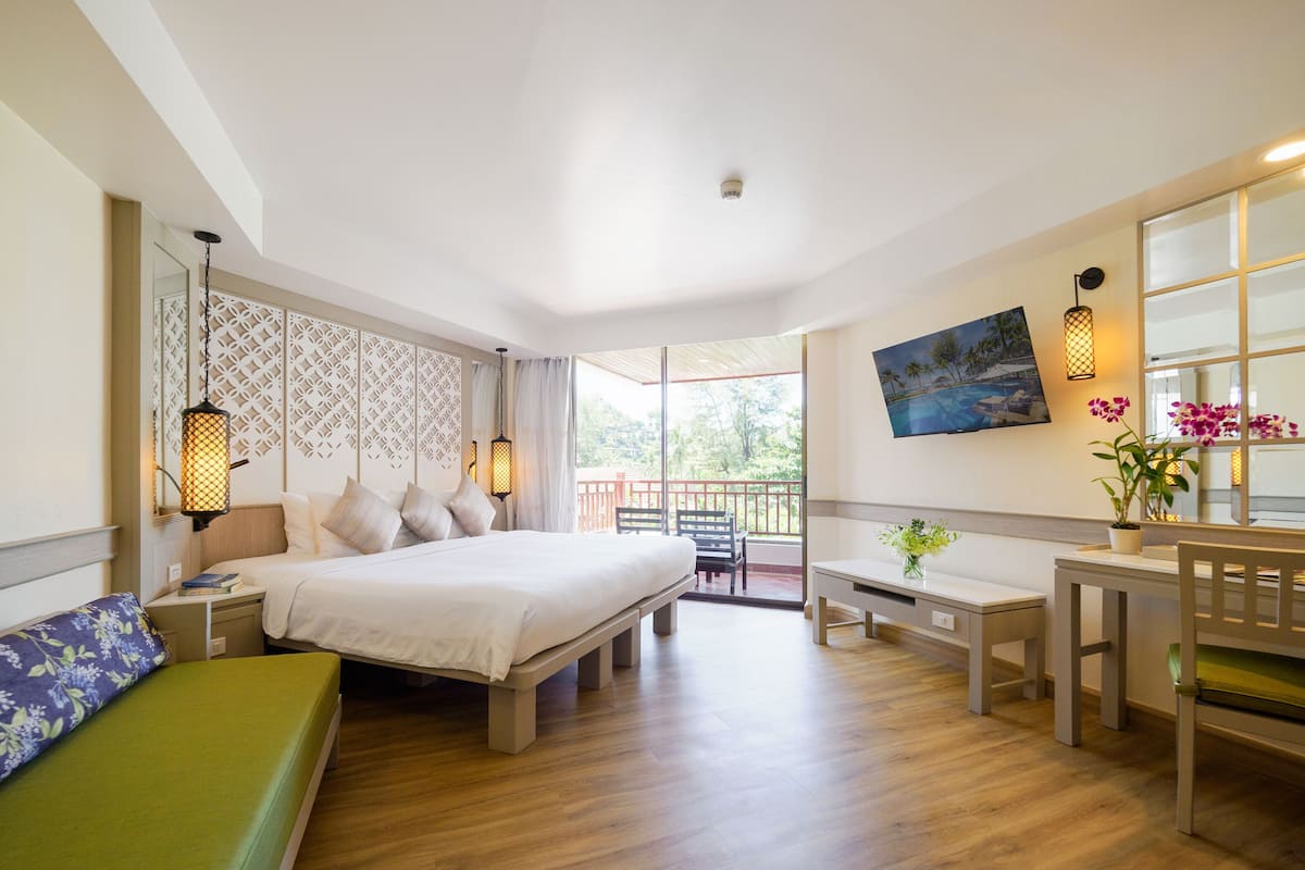 Ein modernes Hotelzimmer mit einem großen Bett, einem Schreibtisch, einem Sessel, einer Bank und einem Balkon mit Blick.
